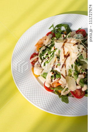 Fresh salad with greens, tomatoes, grilled shrimps on white plate. Top view on yellow background. 111727674
