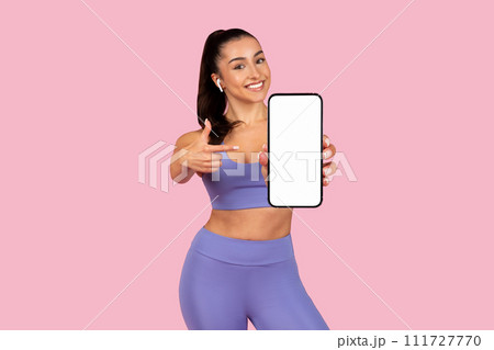 Cheerful woman showing smartphone screen, wearing gym clothes 111727770