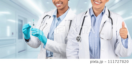 Two happy medical professionals in white coats, one preparing a syringe and the other giving a thumbs up 111727820