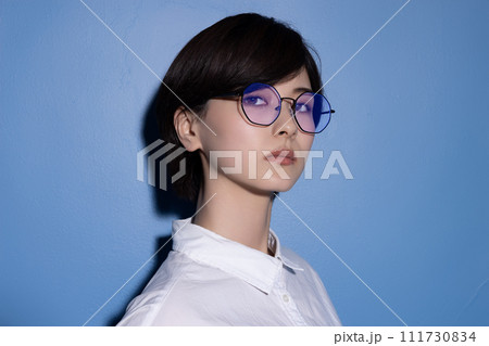 青背景で撮影をした眼鏡をかけた若い女性 青背景で撮影をした眼鏡をかけた若い女性 111730834