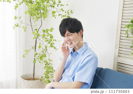 リビングで虫歯が痛む男性 111730883