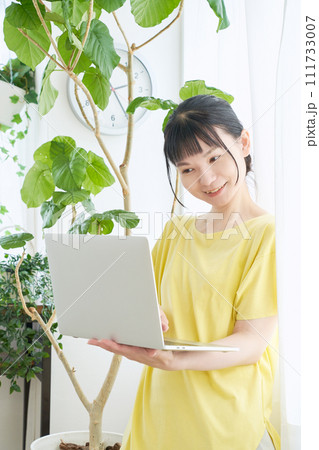 窓辺でパソコンを操作する女性 111733007