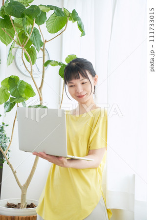 窓辺でパソコンを操作する女性 111733015