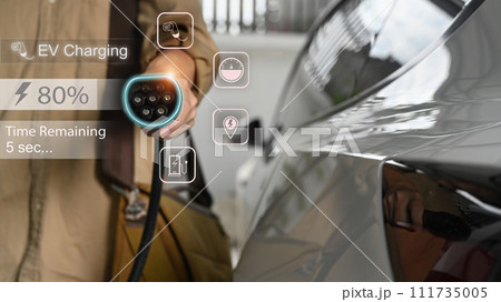 Businessman holding an electric vehicle charging gun connector standing in home garage Businessman holding an electric vehicle charging gun connector standing in home garage 111735005