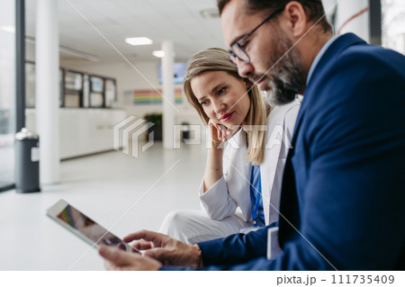 Pharmaceutical sales representative talking with doctor in clinic lobby. Ambitious male sales representative presenting new medication, drugs, showing data on tablet. 111735409