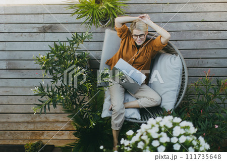 Top view of woman working outdoors in the garden, with laptop on legs. Businesswoman working remotely from homeoffice, thinking about new business or creative idea. Top view of woman working outdoors in the garden, with laptop on legs. Businesswoman working remotely from homeoffice, thinking about new business or creative idea. 111735648