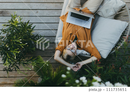 Top view of woman working outdoors in the garden, with laptop on legs. Businesswoman working remotely from homeoffice, thinking about new business or creative idea. Top view of woman working outdoors in the garden, with laptop on legs. Businesswoman working remotely from homeoffice, thinking about new business or creative idea. 111735651