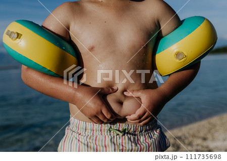 Boy at beach holding his belly fat, body shaming young childrens. Boy at beach holding his belly fat, body shaming young childrens. 111735698