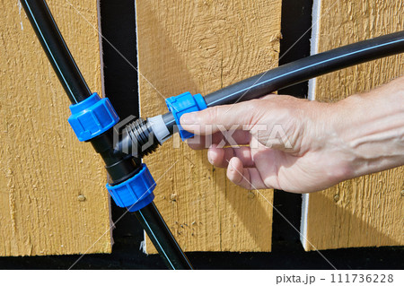 Plumber screws clamping nut onto tightening ring of compression tee fitting when installing an external drinking and irrigation water supply in rural area. Plumber screws clamping nut onto tightening ring of compression tee fitting when installing an external drinking and irrigation water supply in rural area. 111736228