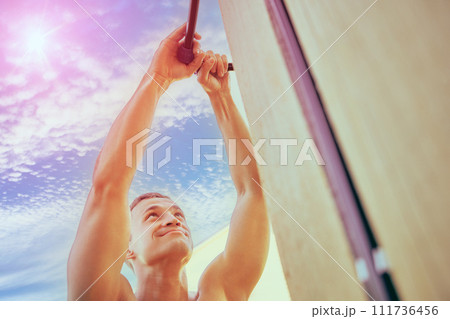 Fixing leak in an outdoor plumbing system, man tightens nut of compression fitting, shirtless white male repairs pipeline outside suburban home. 111736456