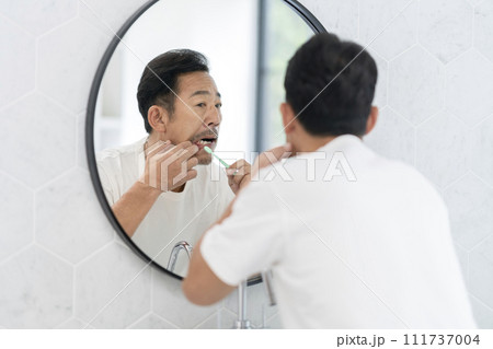 歯磨きをしながら歯茎をチェックする中年男性 歯磨きをしながら歯茎をチェックする中年男性 111737004