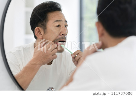 歯磨きをしながら歯茎をチェックする50代の男性 111737006