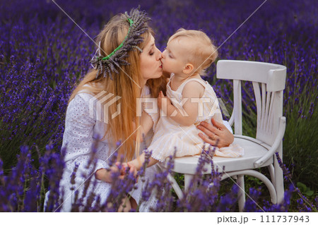 a mother in a lavender wreath kisses her daughter, who is sitting on a white chair a mother in a lavender wreath kisses her daughter, who is sitting on a white chair 111737943