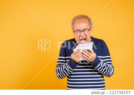 Asian elder man cold having flu and sneezing from sickness virus problem use tissue studio shot isolated on yellow background, Portrait senior old man blowing nose with tissue, pensioner unwell 111738257