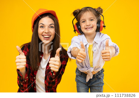 Mother and daughter in accessories for construction, on a yellow background. Mother and daughter in accessories for construction, on a yellow background. 111738826