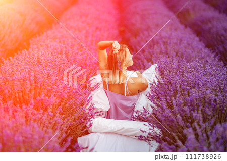 Woman lavender field. A middle-aged woman sits in a lavender field and enjoys aromatherapy. Aromatherapy concept, lavender oil, photo session in lavender 111738926
