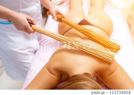 Woman masseuse doing double samurai massage with bamboo brooms in spa. Relaxing massage concept Woman masseuse doing double samurai massage with bamboo brooms in spa. Relaxing massage concept 111738928