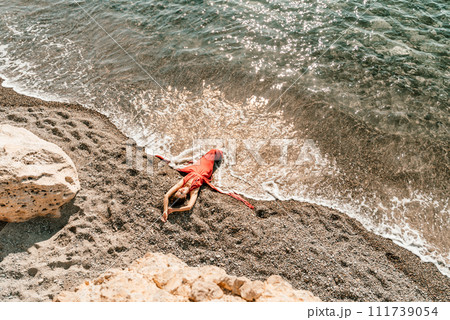Woman red dress sea. Female dancer in a long red dress posing on a beach with rocks on sunny day Woman red dress sea. Female dancer in a long red dress posing on a beach with rocks on sunny day 111739054