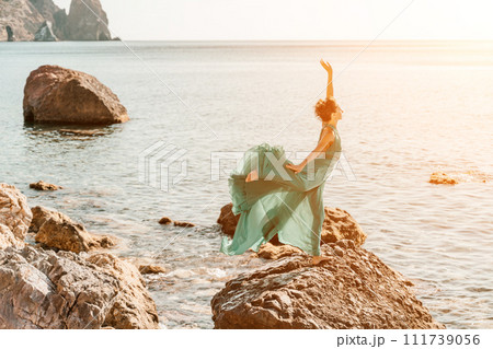 Woman green dress sea. Woman in a long mint dress posing on a beach with rocks on sunny day. Girl on the nature on blue sky background. 111739056