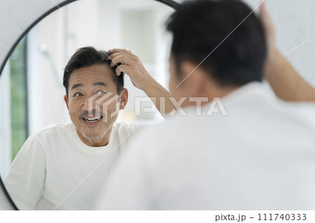 鏡を見ながら髪に触る笑顔の50代の男性 111740333