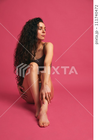 Slender smooth legs. Young beautiful slim brunette girl posing in underwear against pink studio background. Slender smooth legs. Young beautiful slim brunette girl posing in underwear against pink studio background. 111740472