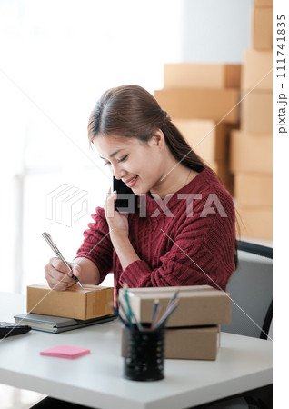 Startup SME small business entrepreneur of freelance Asian woman wearing apron using laptop and box to receive and review orders online to prepare to pack sell to customers, online sme business ideas. Startup SME small business entrepreneur of freelance Asian woman wearing apron using laptop and box to receive and review orders online to prepare to pack sell to customers, online sme business ideas. 111741835