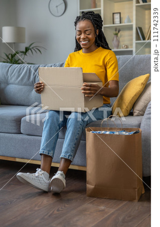 Young woman opening delivery from online shop and looking contented Young woman opening delivery from online shop and looking contented 111742339