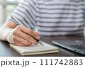 Close-up of hand writing on blank notebook on table. 111742883