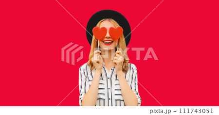 Portrait of happy cheerful young woman with sweet red heart shaped lollipop on stick on pink Portrait of happy cheerful young woman with sweet red heart shaped lollipop on stick on pink 111743051