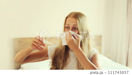 Sick woman sneezing blow nose using tissue measuring checking body temperature with thermometer Sick woman sneezing blow nose using tissue measuring checking body temperature with thermometer 111743057