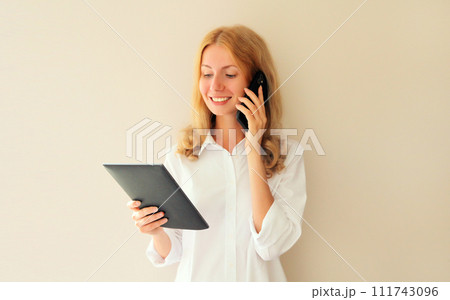 young woman employee with digital tablet computer calling on mobile phone in office young woman employee with digital tablet computer calling on mobile phone in office 111743096