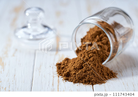 cinnamon powder poured out of a storage jar on a white wooden table. cinnamon powder poured out of a storage jar on a white wooden table. 111743404