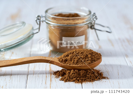 cinnamon powder poured out of a wooden spoon on a white wooden table, selective focus. 111743420
