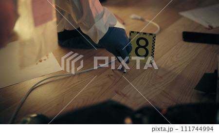 A forensic expert in protective gear is collecting evidence into a plastic bag after taking photos A forensic expert in protective gear is collecting evidence into a plastic bag after taking photos 111744994