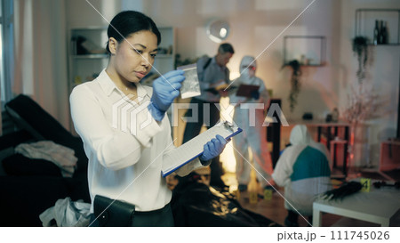 A black female detective is describing a bag with a substance in her report at the crime scene A black female detective is describing a bag with a substance in her report at the crime scene 111745026