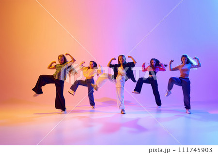 Dynamic image of talented, artistic teen girls dancing hip hop against gradient studio background in neon light 111745903