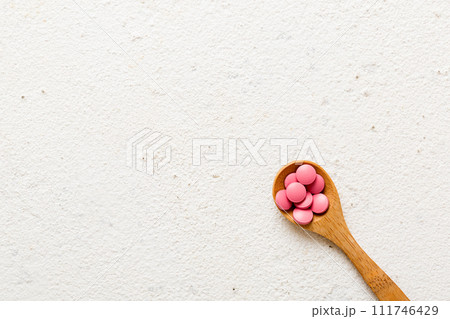 Vitamin capsules in a spoon on a colored background. Pills served as a healthy meal. Red soft gel vitamin supplement capsules on spoon 111746429