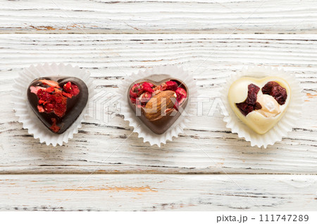chocolate sweets in the form of a heart with fruits and nuts on a colored background. top view with space for text, holiday concept 111747289