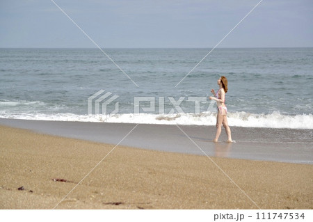 波打ち際を歩くビキニの水着を着た若い女性 波打ち際を歩くビキニの水着を着た若い女性 111747534