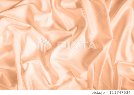 Waves and patterns of crumpled natural satin fabric. Color of the year 2024 Peach Fuzz 111747634