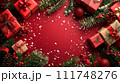 Festive Christmas composition with red gifts, pine branches, and holiday ornaments on a red background with snowflakes. 111748276