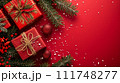 Red Christmas gifts tied with ribbons and baubles nestled among pine branches on a vibrant red background with snowflakes. 111748277