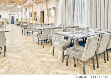 Side view of a large empty bright restaurant with tables, soft chairs, curtains and a wooden floor. Modern interior of a cafe, restaurant for events, holidays, weddings, birthdays with copy space. Side view of a large empty bright restaurant with tables, soft chairs, curtains and a wooden floor. Modern interior of a cafe, restaurant for events, holidays, weddings, birthdays with copy space. 111748719