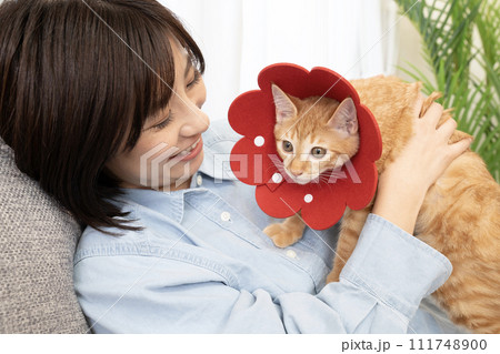赤いエリザベスカラーをした仔猫と微笑む女性 111748900