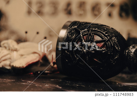 A worn rag doll lies in a haunting occult setting with a Ouija board backdrop, invoking a sense of mystery. 111748983