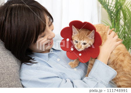 赤いエリザベスカラーをした仔猫と微笑む女性 111748991