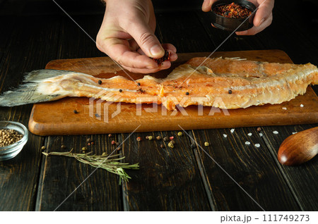 The cook prepares fresh raw fish on a wooden cutting board. Homemade delicious fish dish according to an old recipe with aromatic spices The cook prepares fresh raw fish on a wooden cutting board. Homemade delicious fish dish according to an old recipe with aromatic spices 111749273