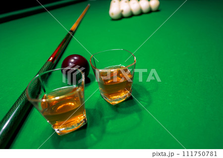 Glass of whiskey on billiard table with cue and billiard balls in background 111750781