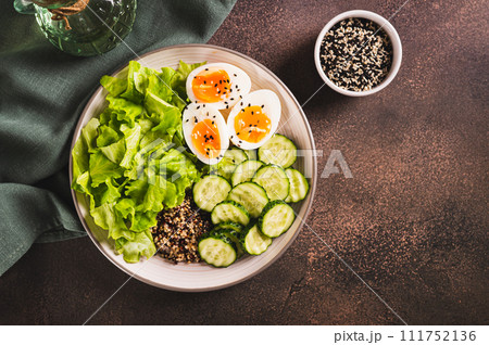 Bowl with quinoa, cucumber, boiled egg, lettuce and sesame seeds on the table top view 111752136