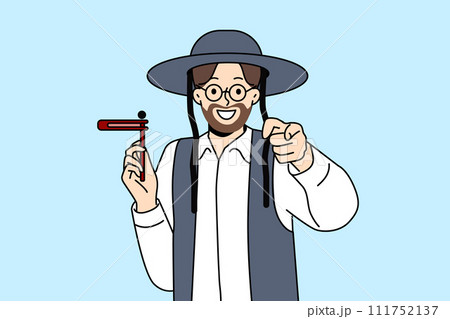 Orthodox jewish man with grager ratchet in hand points finger at screen, during Hanukkah holiday 111752137